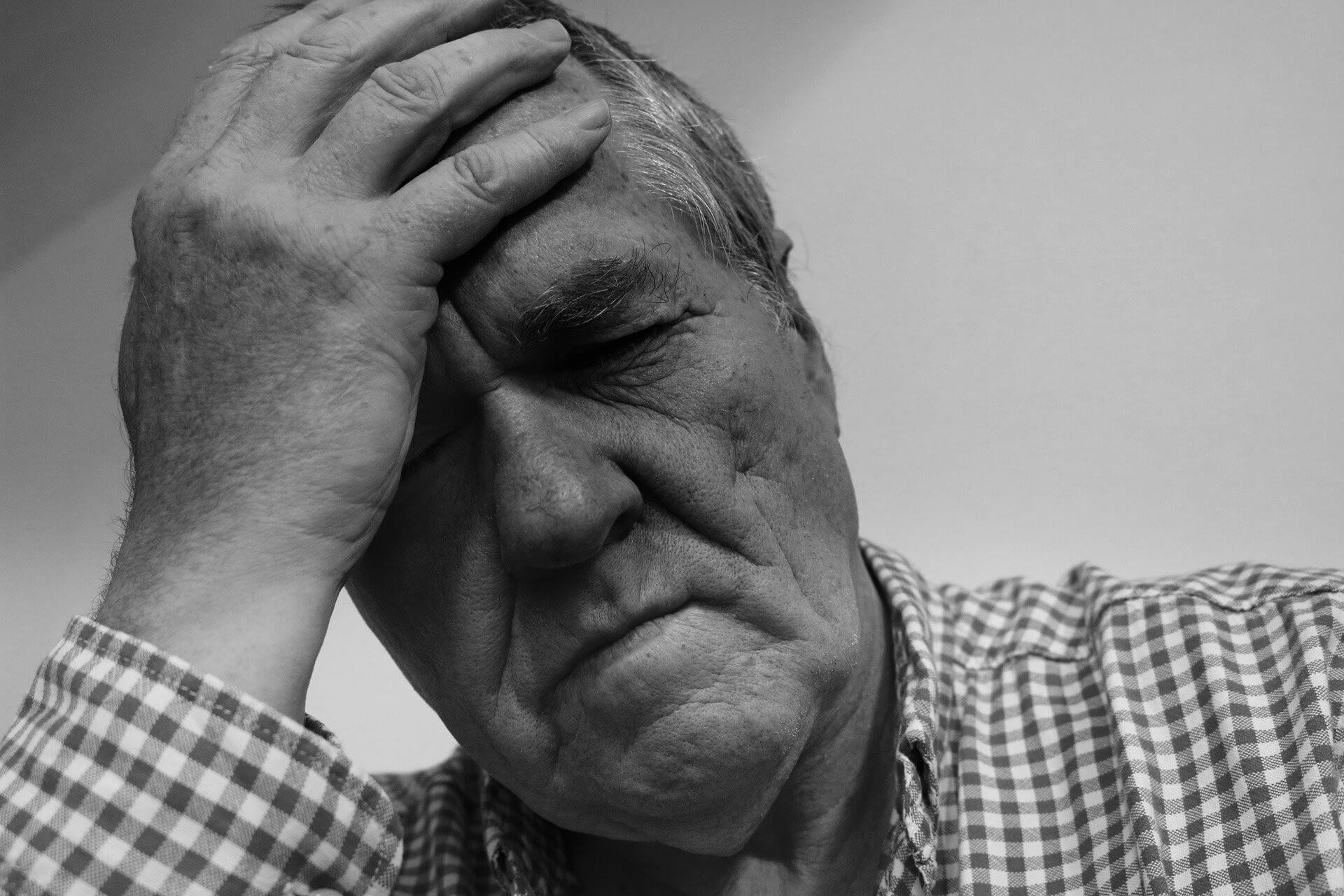 Black and white photo, old man with hand on forehead having a headache