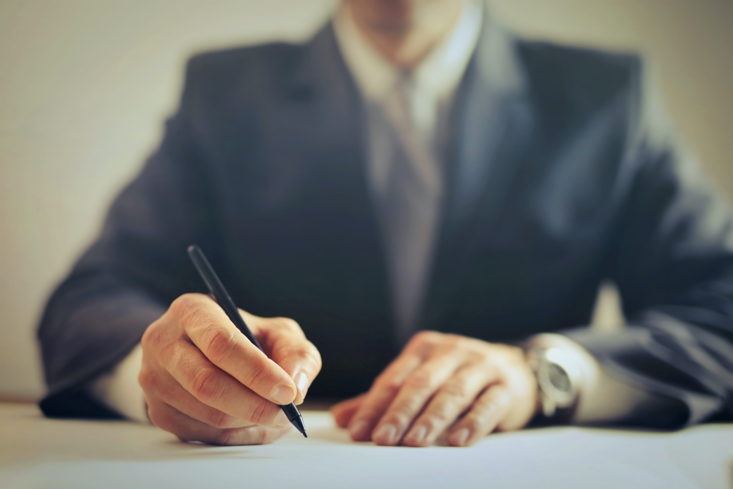 A man from the chest down sitting in a nice suit signing a paper.